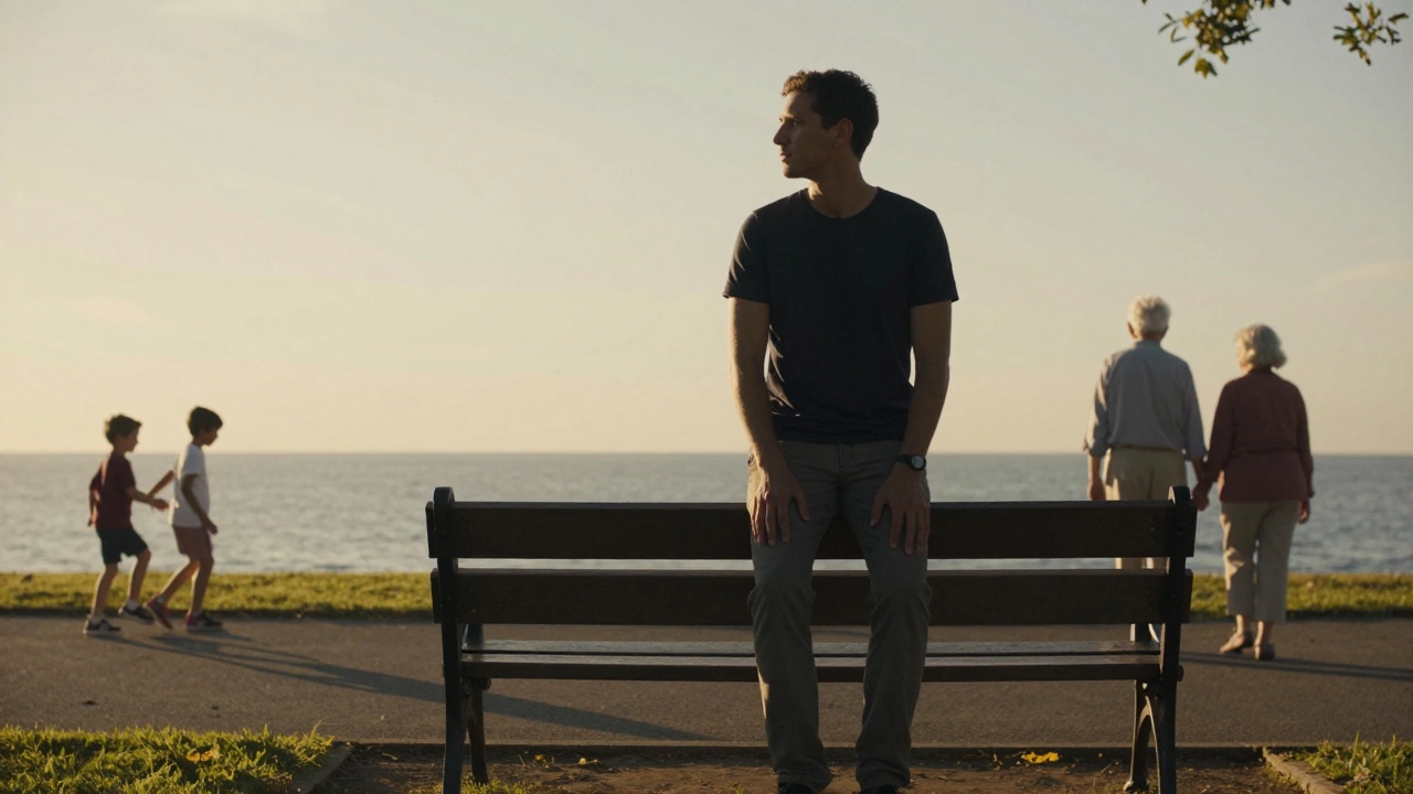 A man sitting alone on a park bench at dusk, calm and still as others move in the background.