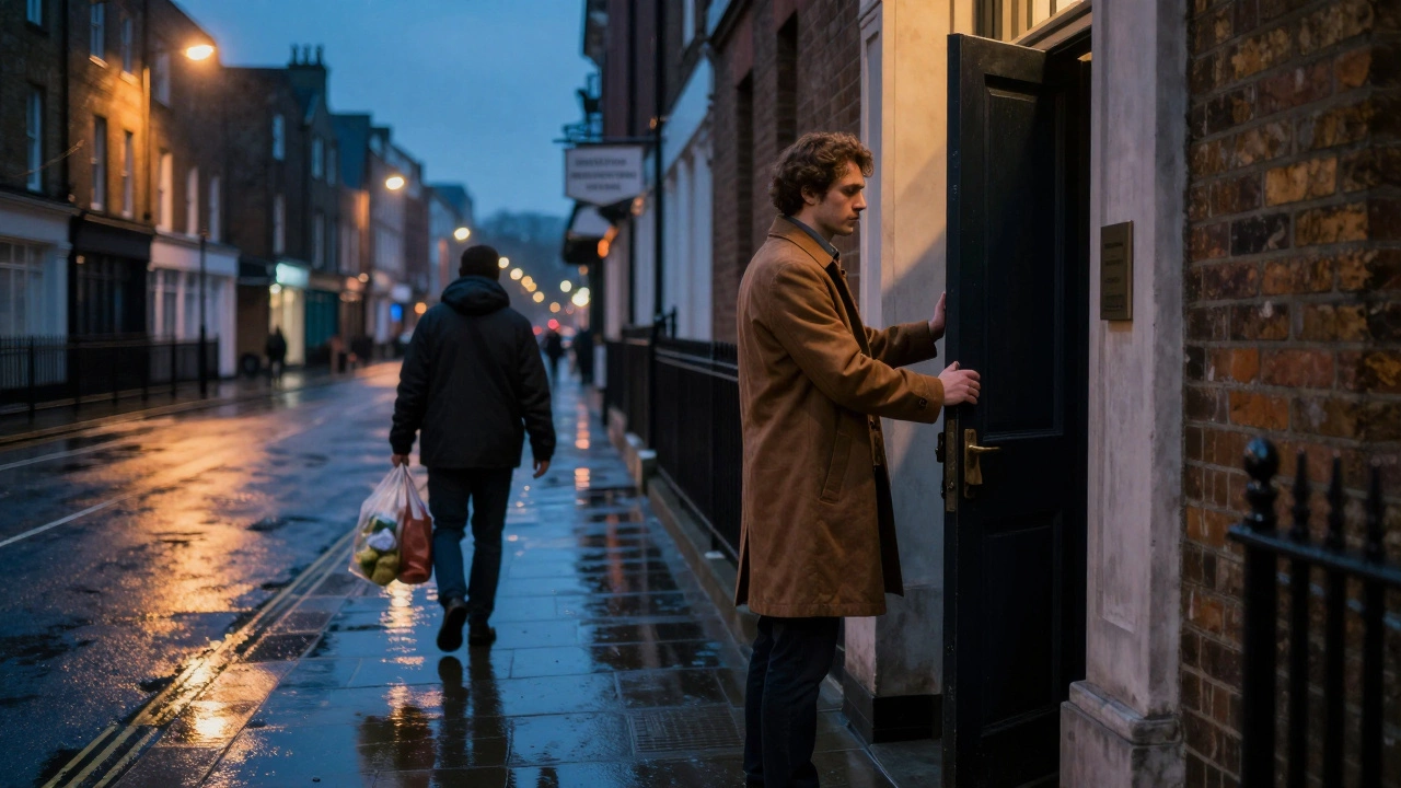 A man holding a door open for a stranger at dusk, city lights reflecting on wet pavement.
